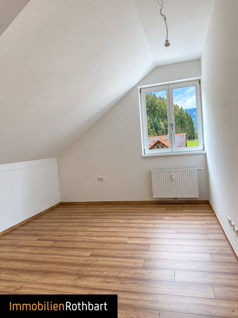 Dachgeschosszimmer mit Laminatboden und Fenster, das einen schönen Blick auf die Berge bietet.