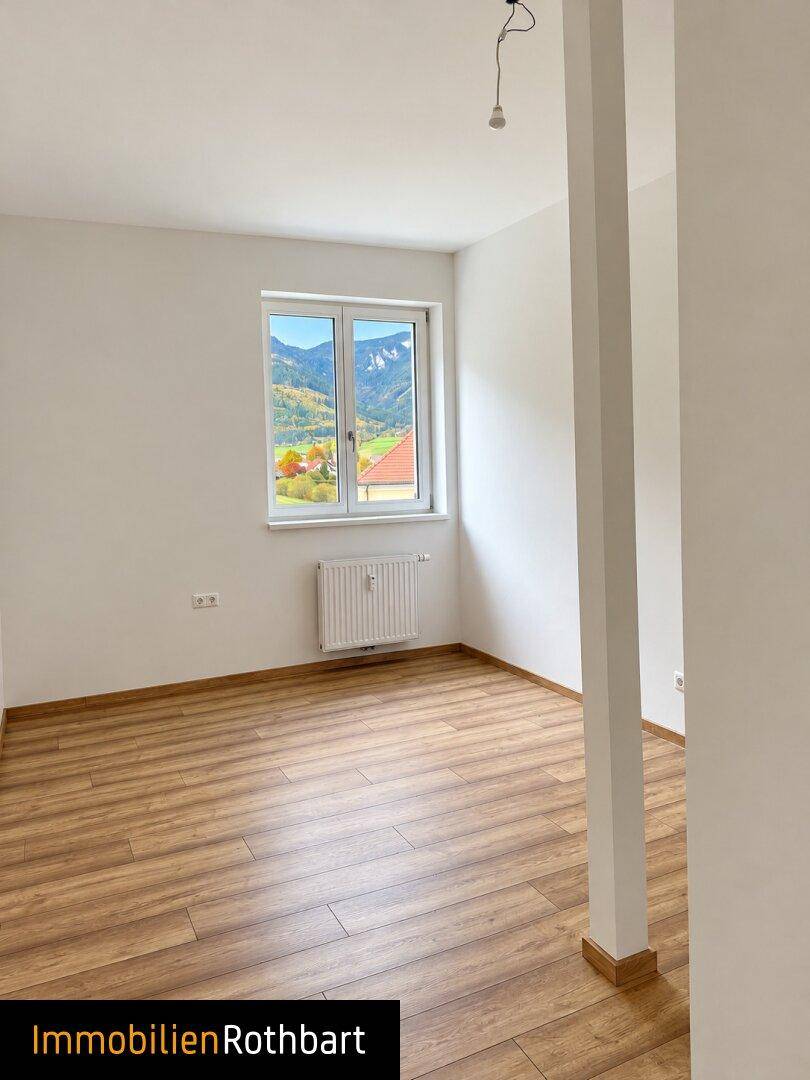 Geräumiger Raum mit Laminatboden und einem Fenster, das einen weiten Blick auf die Berge freigibt.