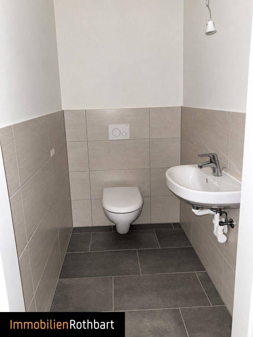 Modernes Gäste-WC mit Wand-WC, Waschbecken und hellgrauen Fliesen an Wänden und Boden.