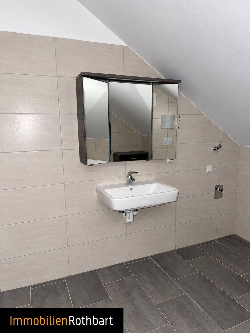 Badezimmer mit modernem Waschbecken, Spiegelschrank und hellen Fliesen an Wänden und Boden.