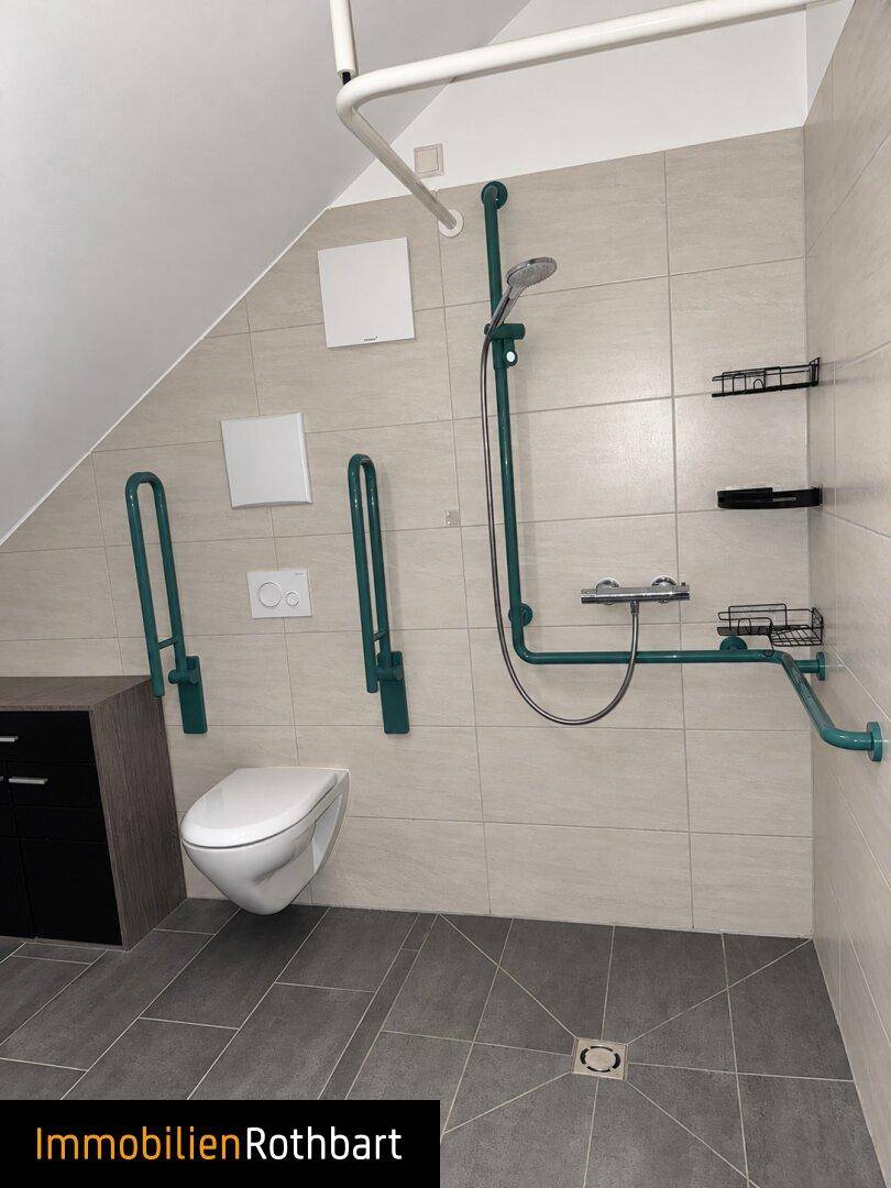Barrierefreies Badezimmer mit Dusche, Wand-WC und Haltegriffen für mehr Sicherheit.