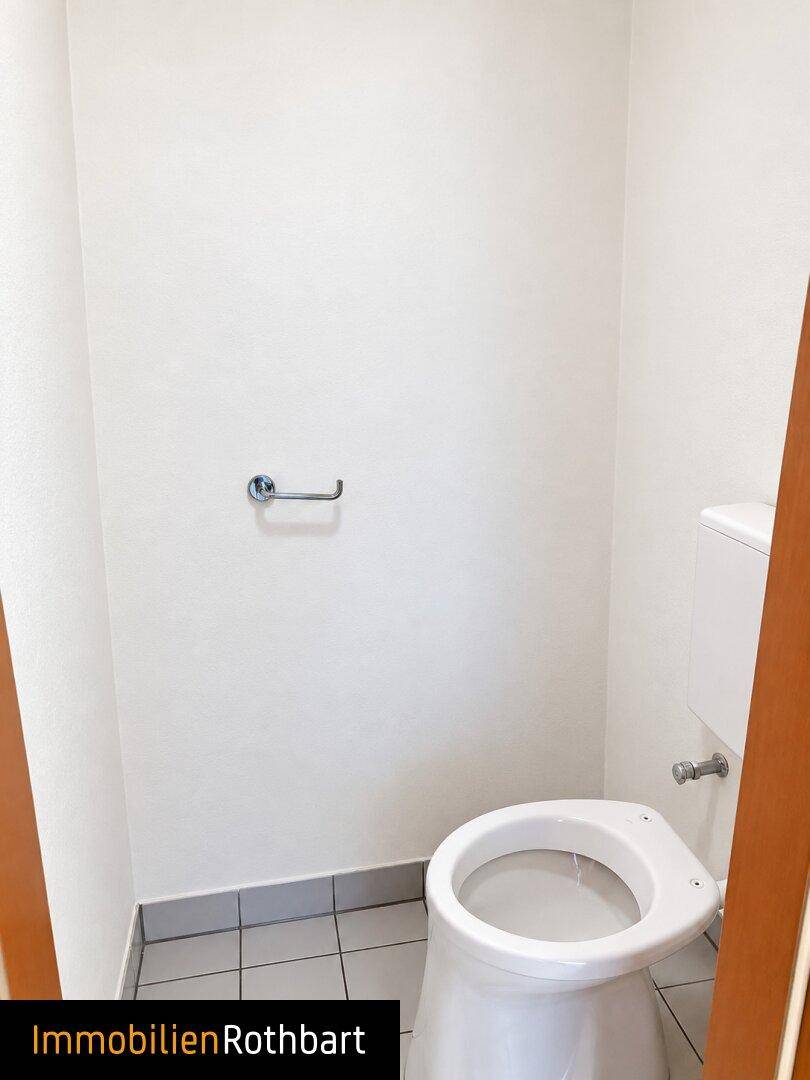 Separates WC mit Toilette und hellgrauen Bodenfliesen, funktional und sauber.