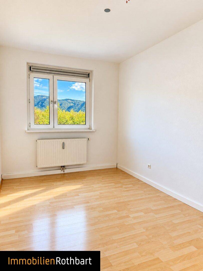 Schlafzimmer mit hellem Parkettboden und Fenster mit schöner Aussicht auf die Berge.