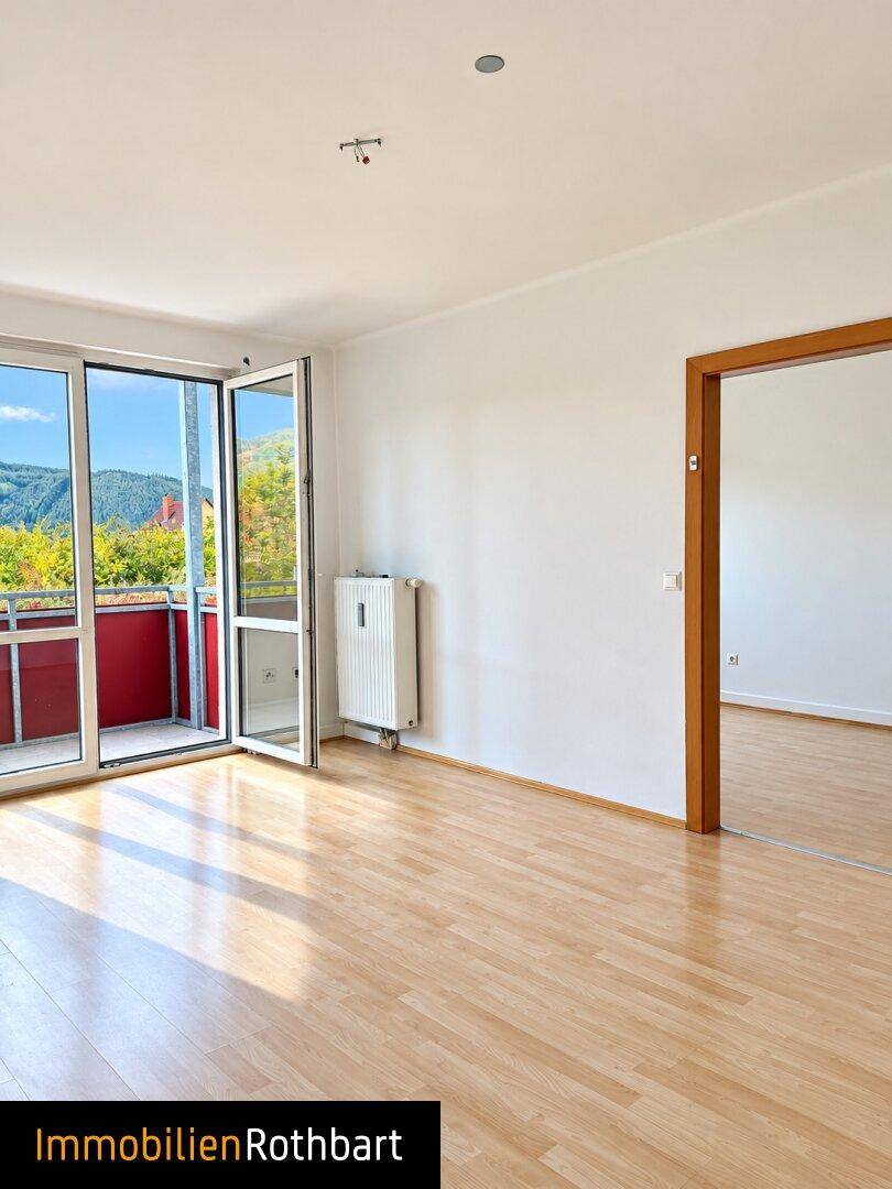 Helles Wohnzimmer mit Parkettboden und Zugang zu einem Balkon mit Bergblick.