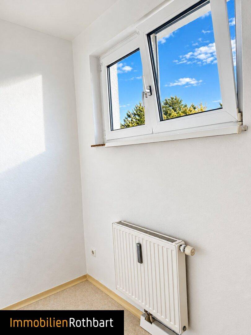 Heller Raum mit weiß gestrichenen Wänden und einem Fenster mit Blick ins Grüne.