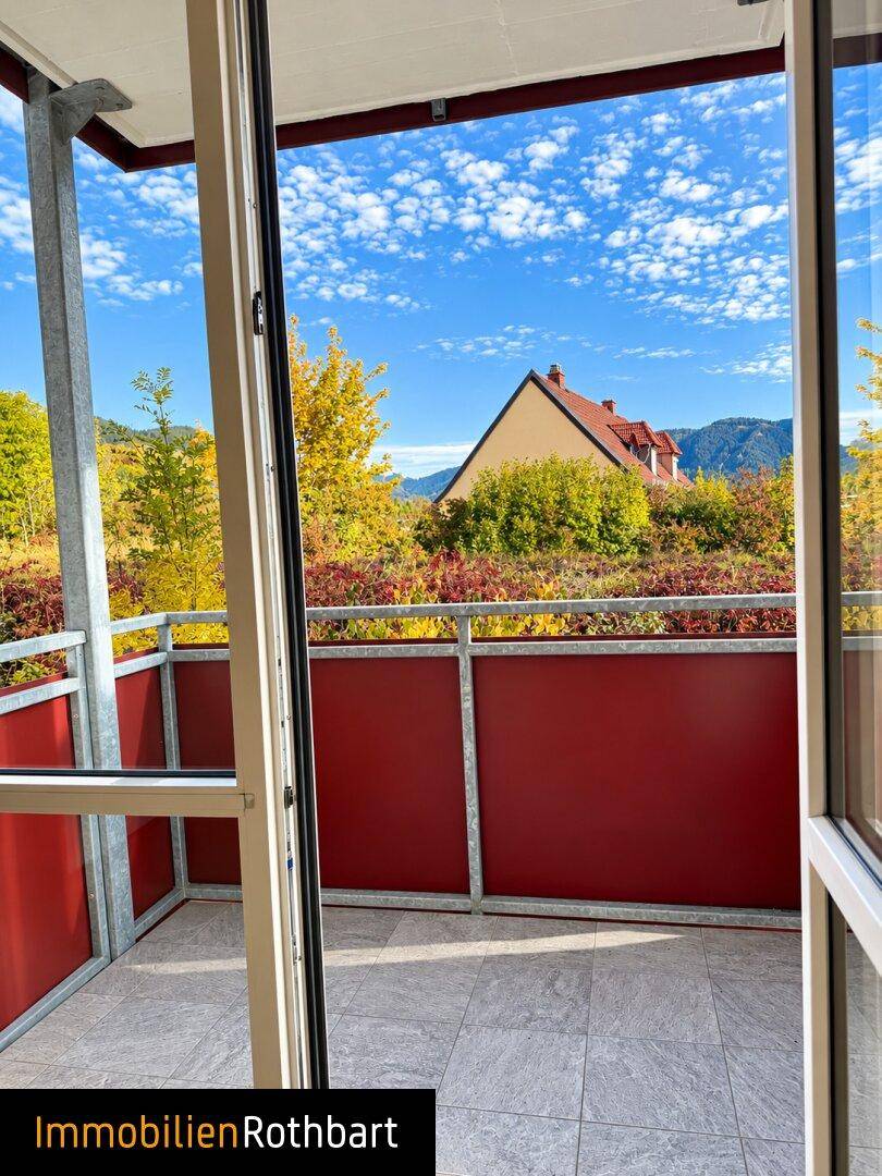 Balkon mit Fliesenboden und roter Brüstung bietet einen weiten Blick ins Grüne.