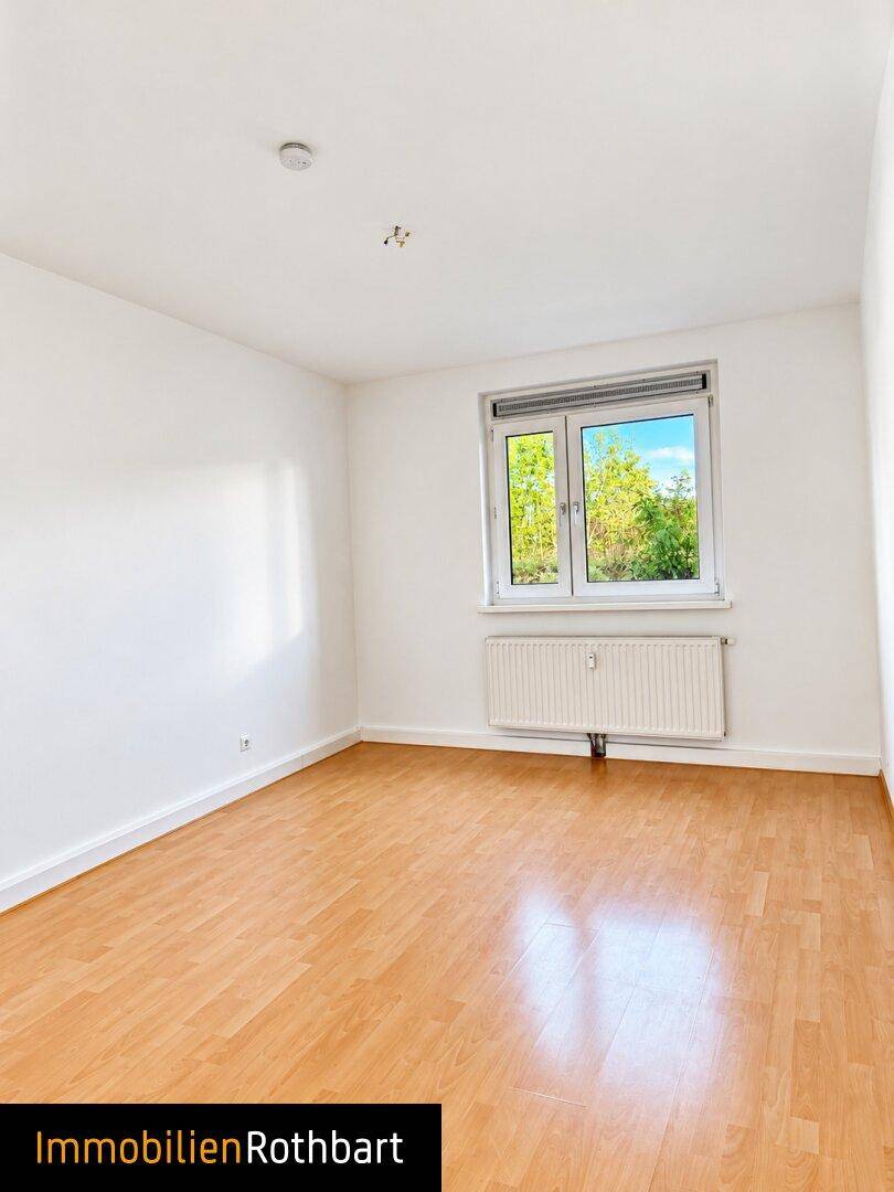 Helles Zimmer mit Laminatboden und Fenster mit Blick ins Grüne.