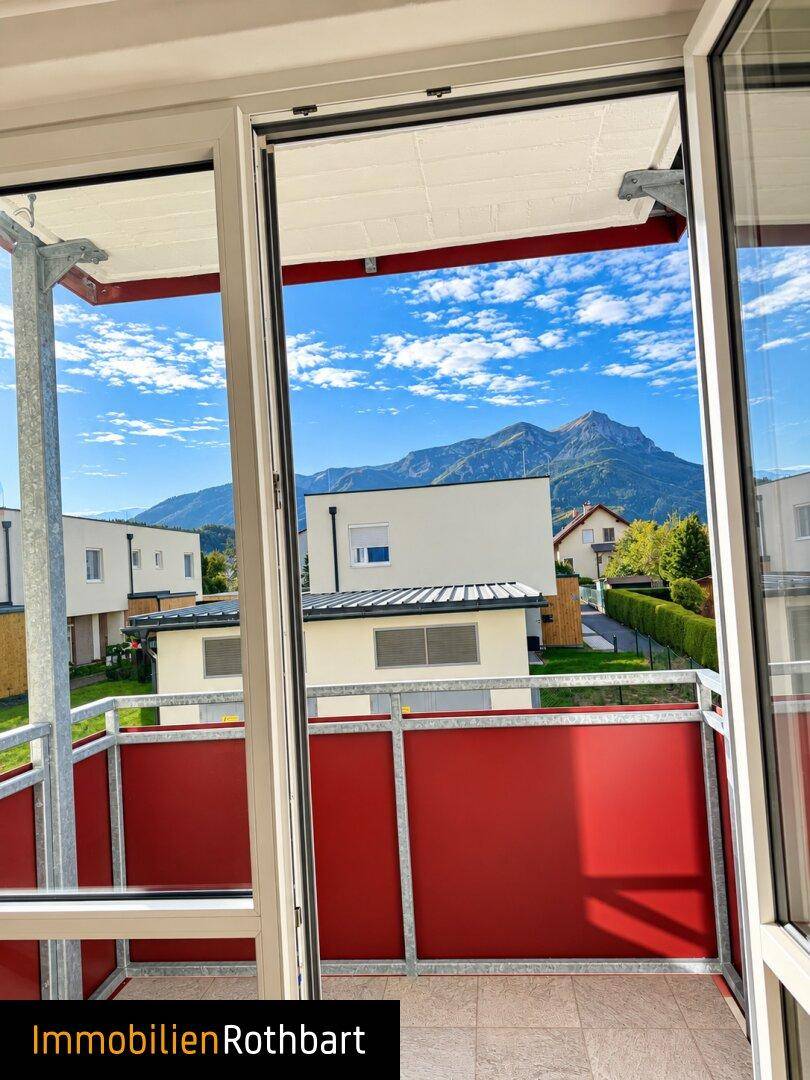 Balkon mit roter Brüstung und weitem Blick auf die umliegenden Berge und Häuser.