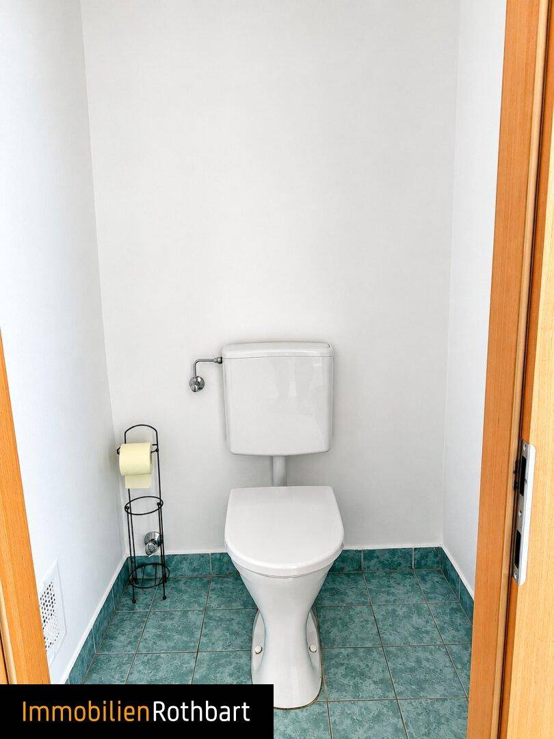 Separates WC mit hellgrünen Fliesen und einfacher Ausstattung.