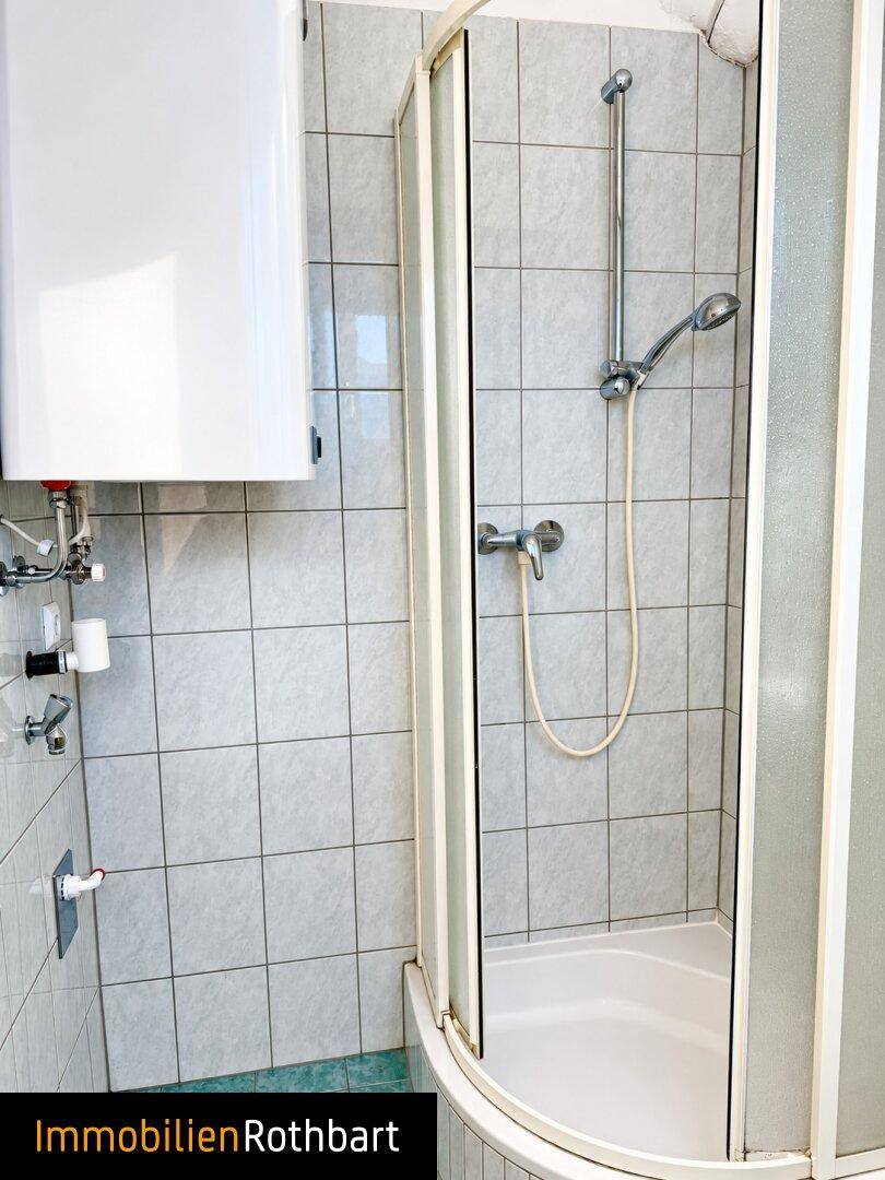 Badezimmer mit Duschkabine und Boiler, ausgestattet mit hellen Wandfliesen.