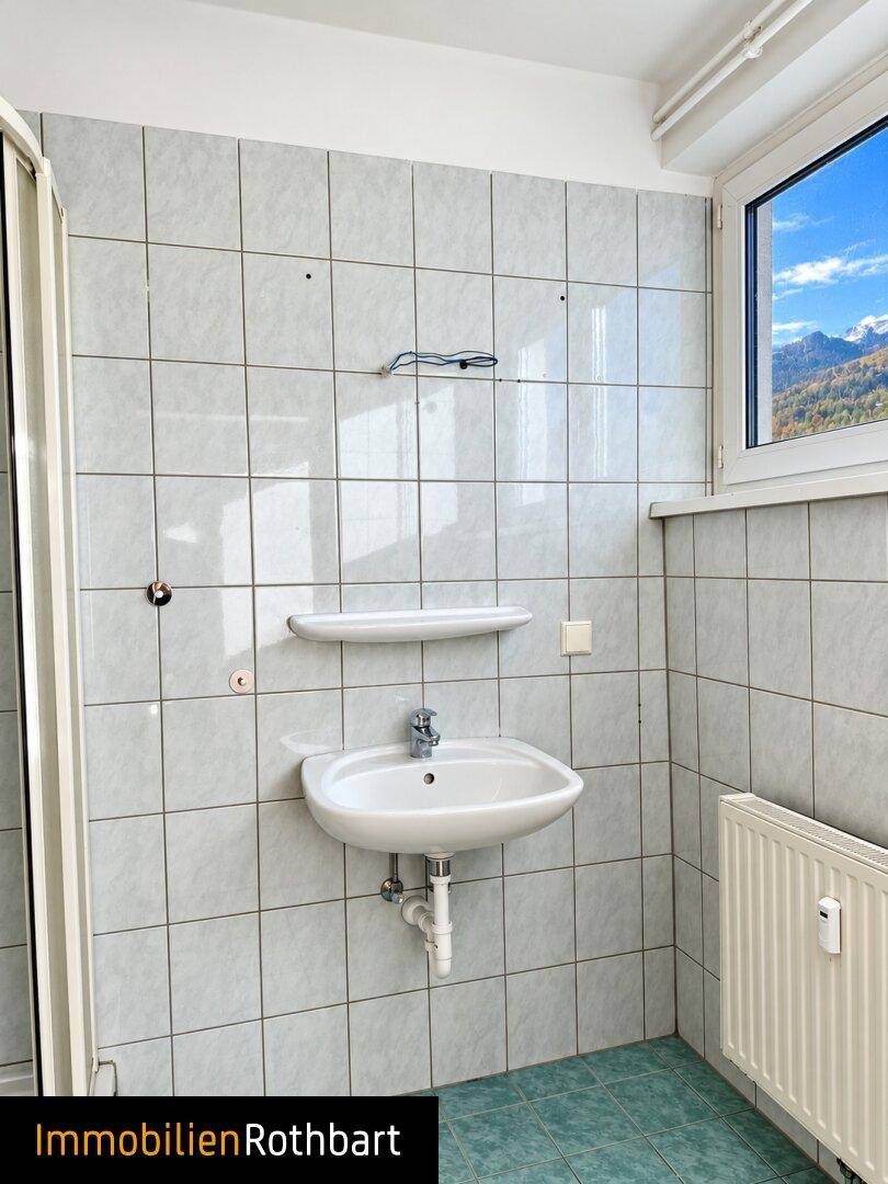 Badezimmer mit Waschbecken, Duschkabine und Fenster mit Bergblick.