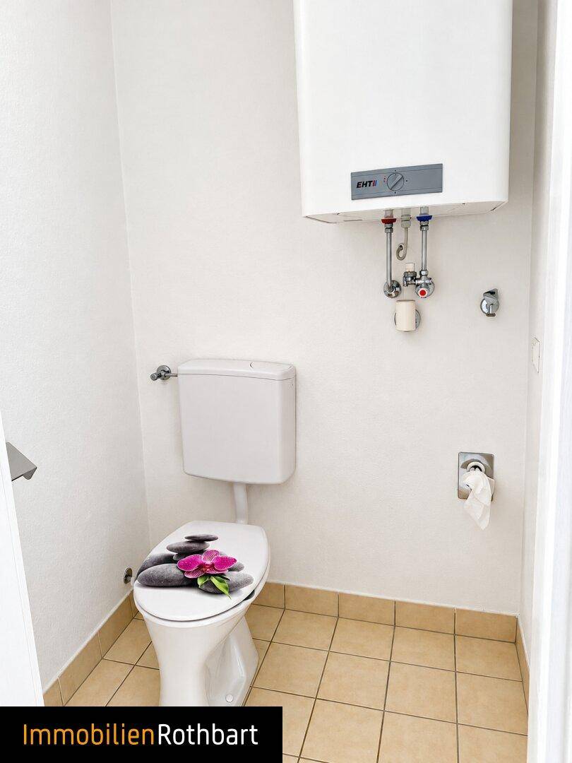 Kleines WC mit Fliesenboden, Toilette und einem Warmwasserboiler an der Wand.