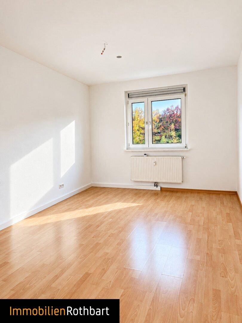 Sonniger Raum mit Laminatboden und einem Fenster, das einen herbstlichen Ausblick bietet.