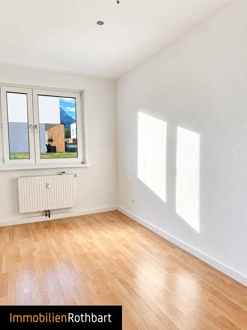 Helles Zimmer mit Laminatboden und einem Fenster, das einen Blick auf die Berge freigibt.
