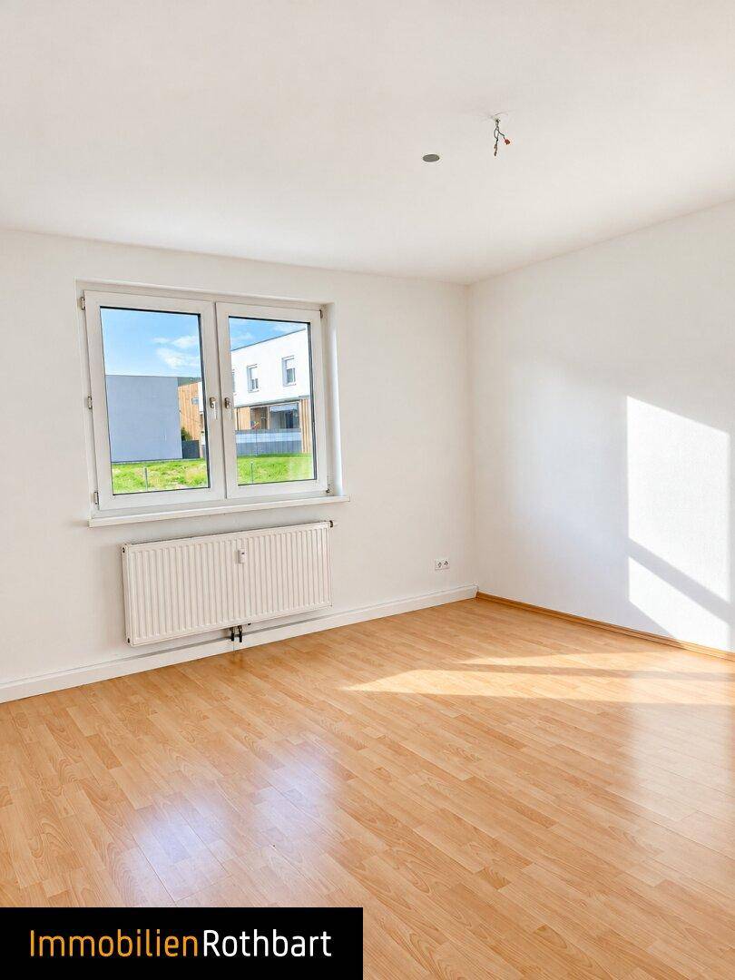 Lichtdurchflutetes Zimmer mit Laminatboden und Blick ins Grüne durch das Fenster.