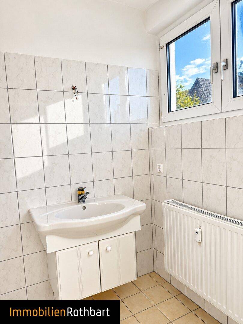 Helles Badezimmer mit Waschbecken, Heizkörper und einem Fenster für Tageslicht.