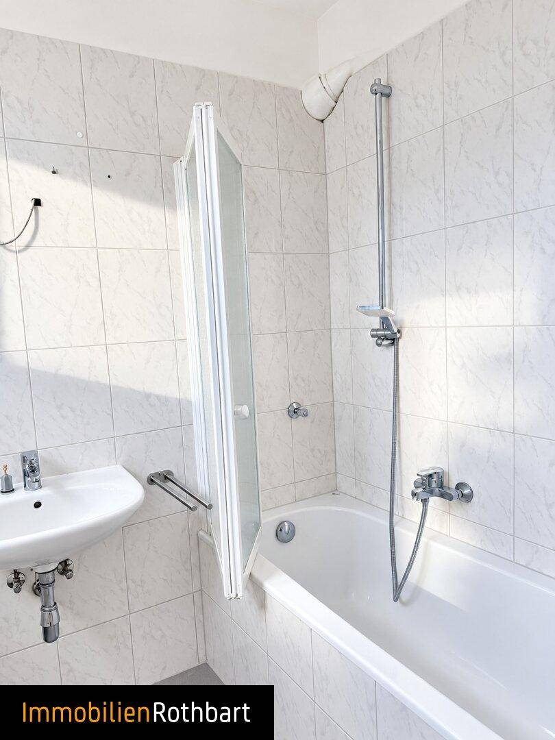 Helles Badezimmer mit Badewanne, Duschvorrichtung und weiß gefliesten Wänden.