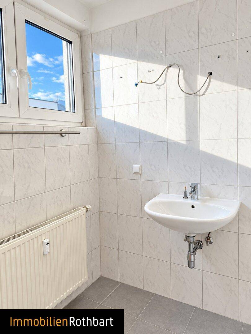 Geräumiges Badezimmer mit Fenster, Waschbecken und Platz für weitere Installationen.