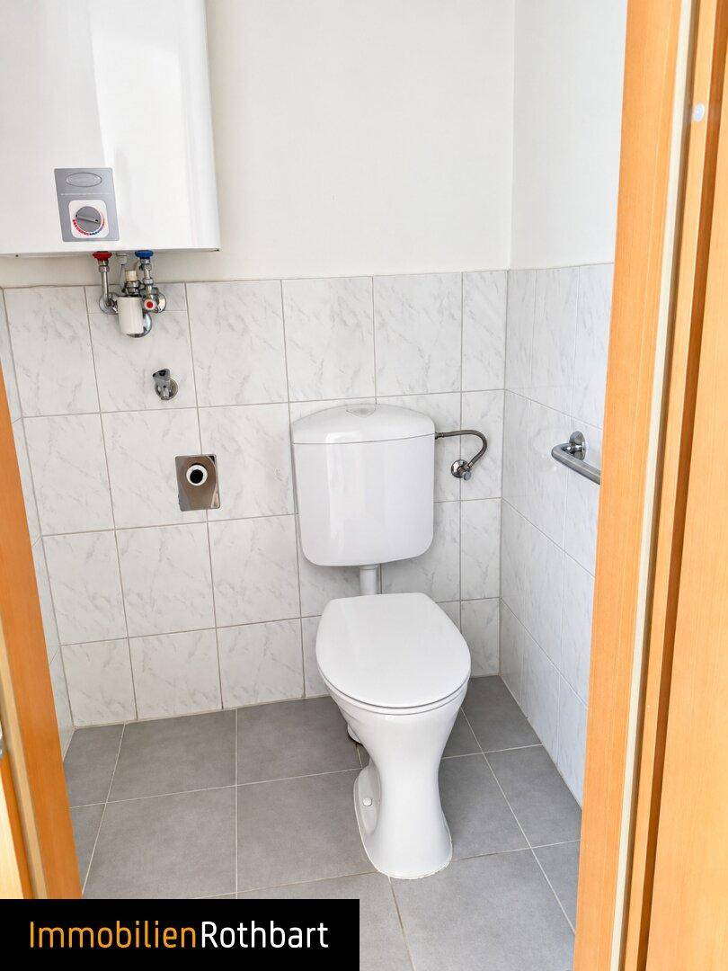 Kleines WC mit Toilette, Boiler und weiß gefliesten Wänden.