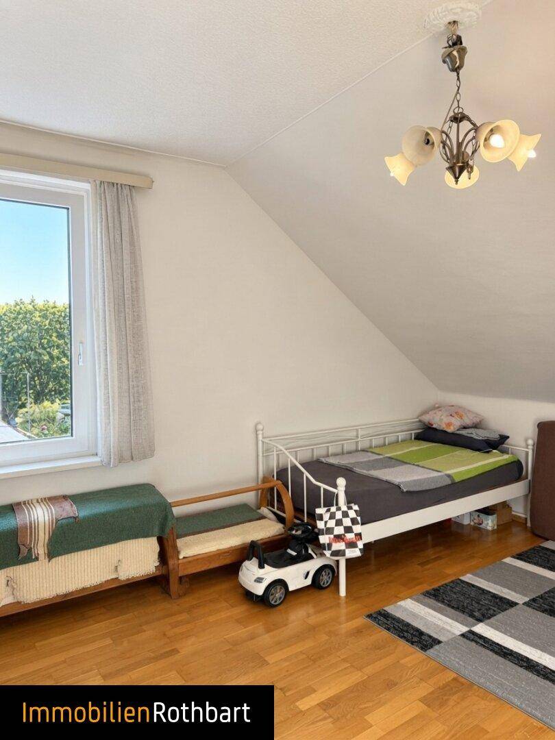 Helles Schlafzimmer mit Einzelbett, Holzboden und Fenster, das einen Blick ins Grüne bietet.