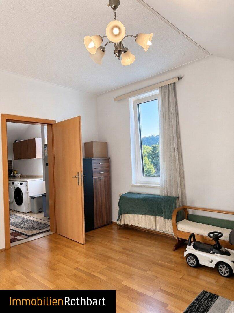 Raum mit Holzboden und Fenster, der Zugang zu einem Bereich mit Waschmaschine bietet.