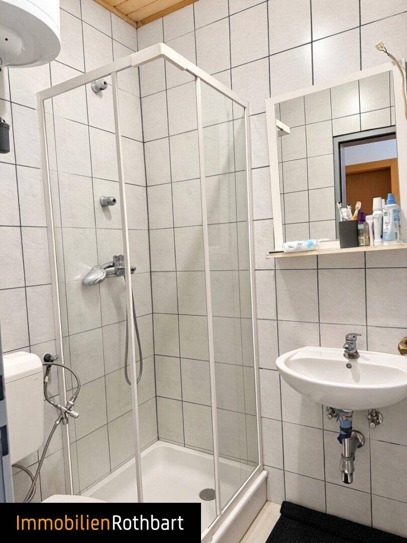 Badezimmer mit weißen Fliesen, Duschkabine und Waschbecken, funktional und hell.