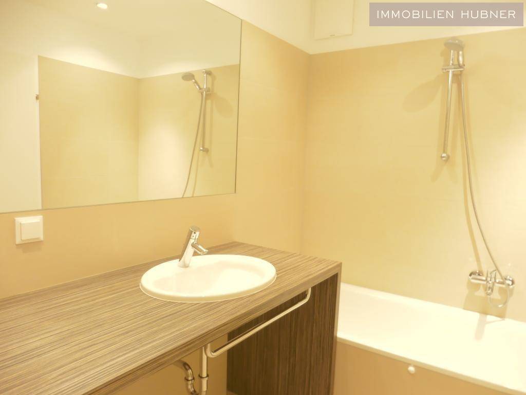 Badezimmer mit Badewanne, Einzelwaschbecken und großem Spiegel, in hellem Design.