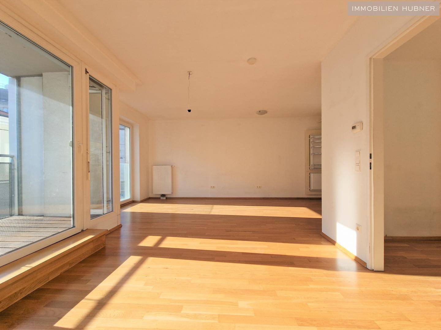 Offener Wohnbereich mit Parkettboden und direktem Zugang zum Balkon.