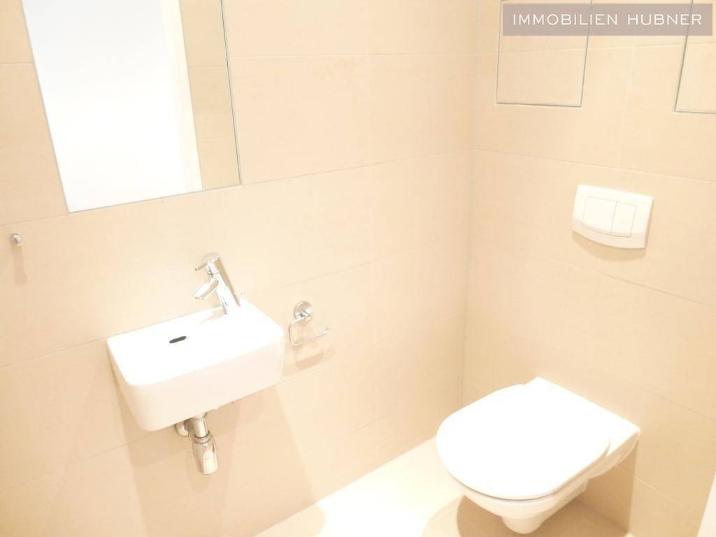 Separates WC mit wandhängender Toilette und kleinem Handwaschbecken.