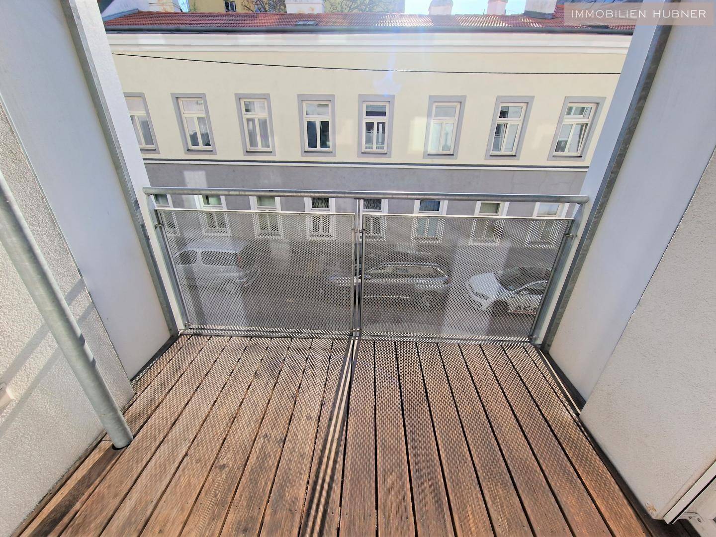 Balkon mit Holzboden und Blick auf die gegenüberliegende Straße und Gebäude.
