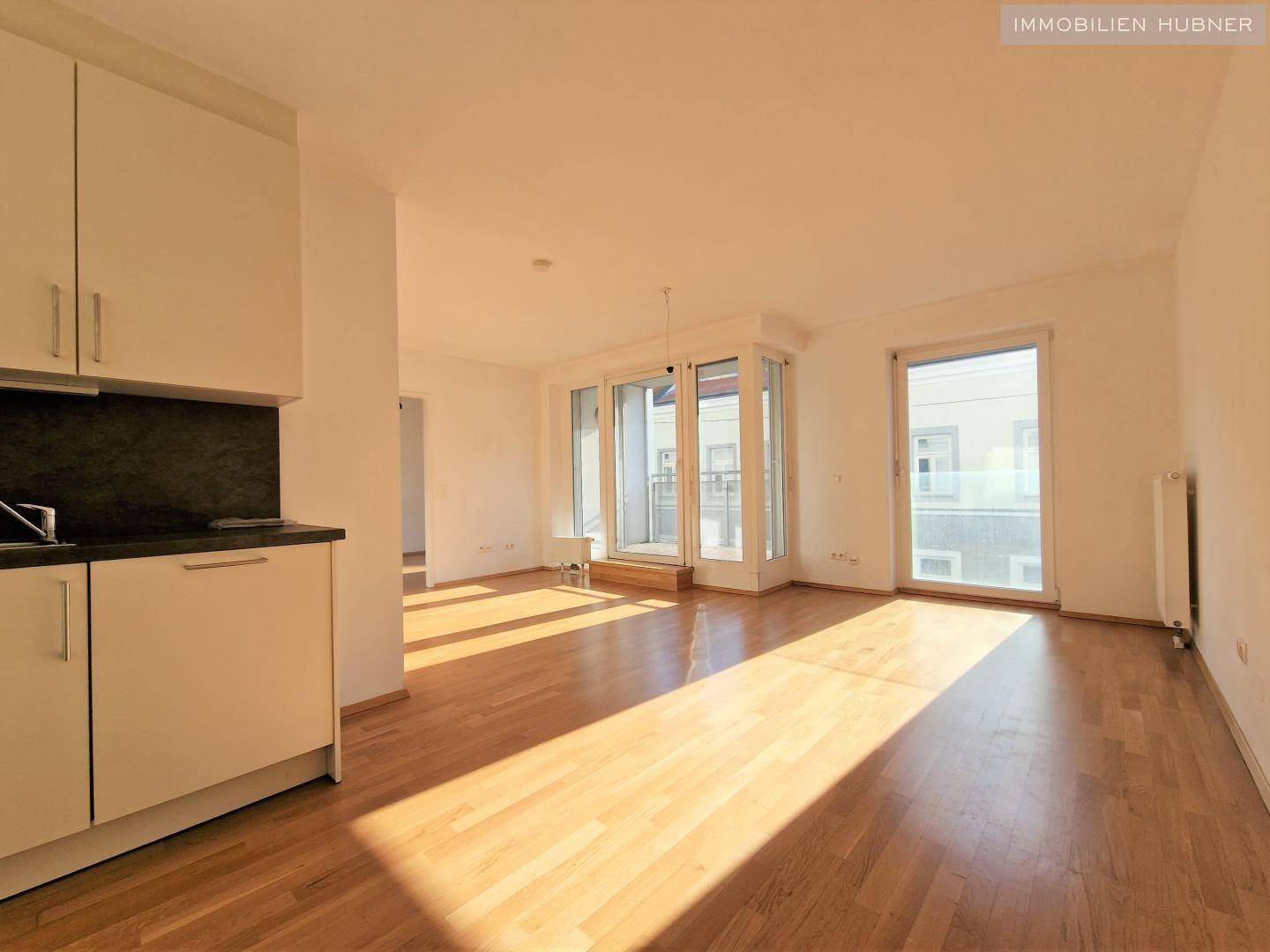 Offener Wohnbereich mit integrierter Küche und Zugang zu einem sonnigen Balkon.