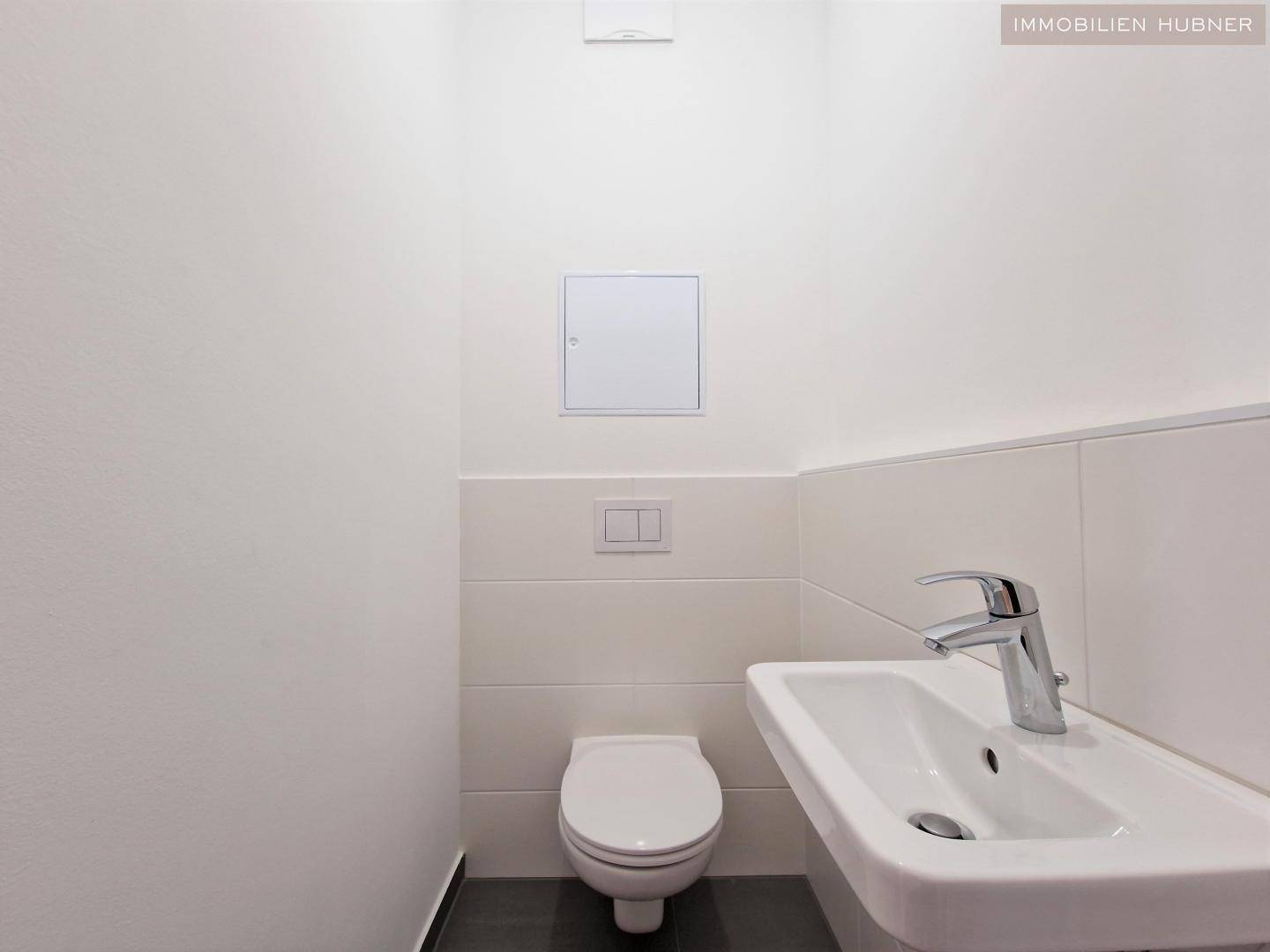 Separates Gäste-WC mit wandhängender Toilette und kleinem Handwaschbecken.
