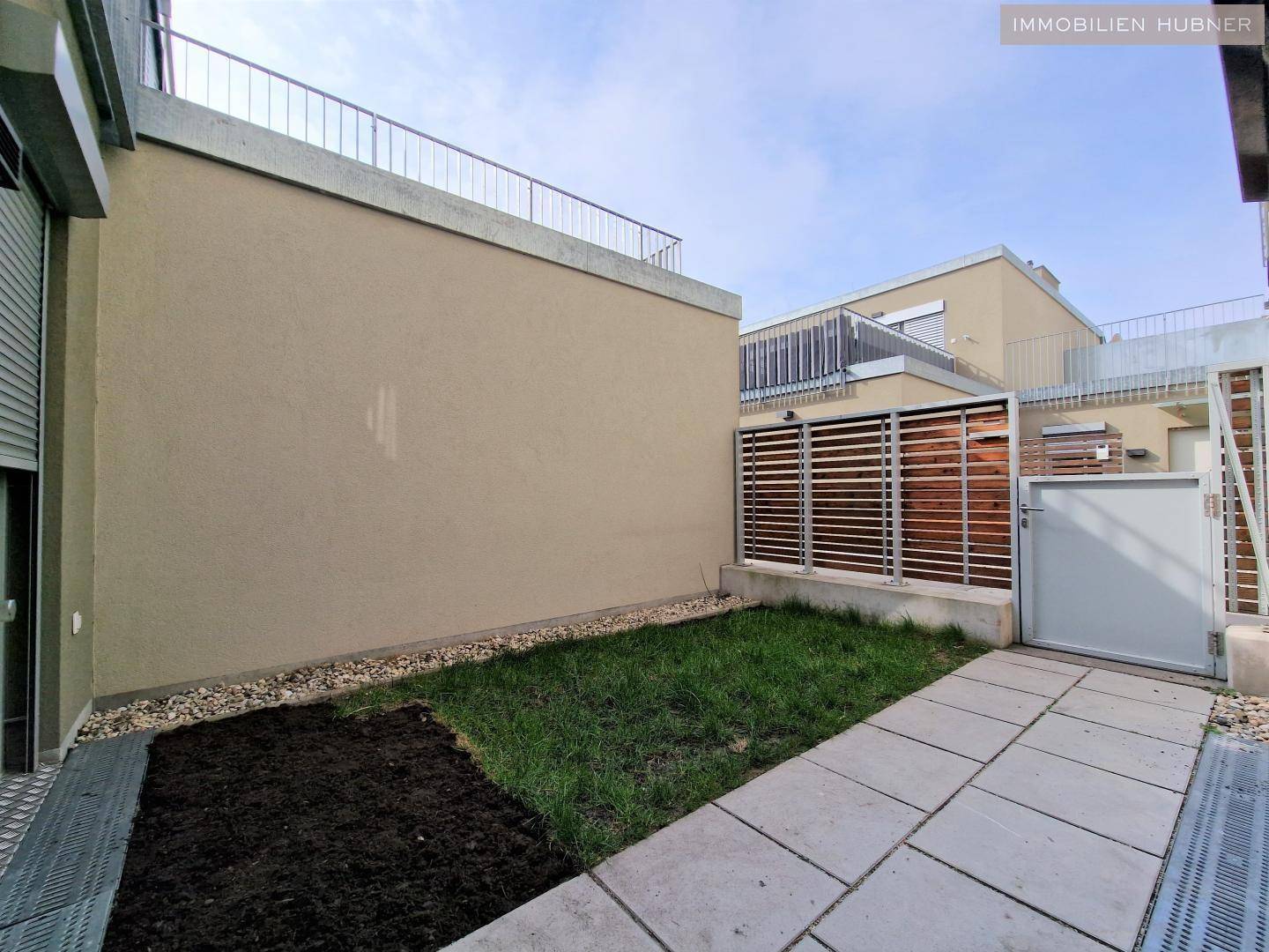 Kleiner privater Gartenbereich mit Rasenfläche, gepflastertem Weg und Sichtschutz.