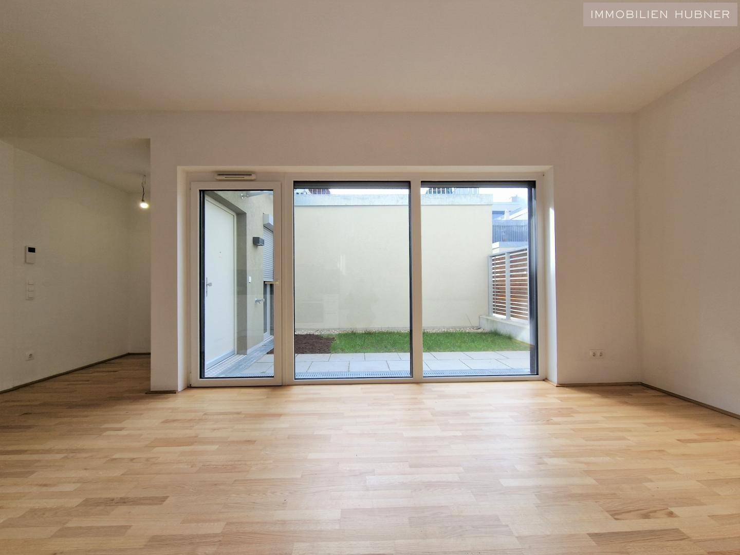 Geräumiger Wohnbereich mit großen Fenstern, Parkettboden und Blick auf den privaten Garten.