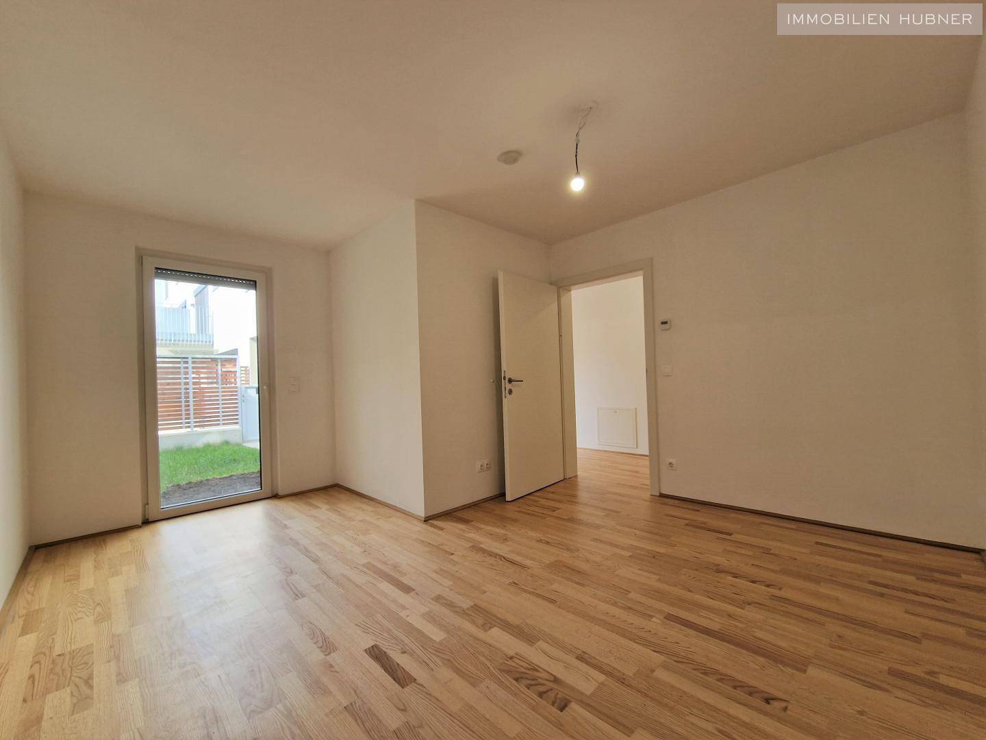Helles Zimmer mit Parkettboden und Zugang zu einem kleinen Außenbereich.