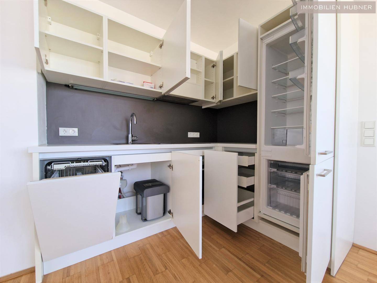 Funktionale Einbauküche mit Geschirrspüler und Kühlschrank, alle Schränke geöffnet für Einblick.