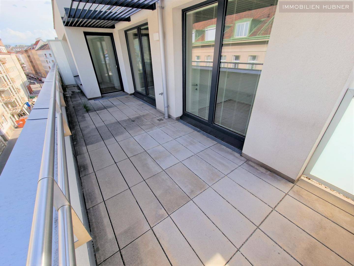 Geräumige Terrasse mit Fliesenboden und großen Glasschiebetüren zum Innenbereich der Wohnung.