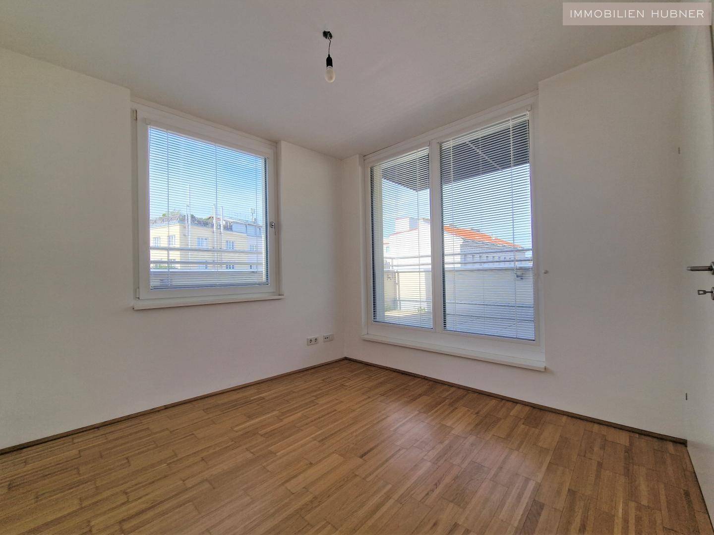 Helles Schlafzimmer mit Parkettboden und großen Fenstern, bereit zur individuellen Einrichtung.