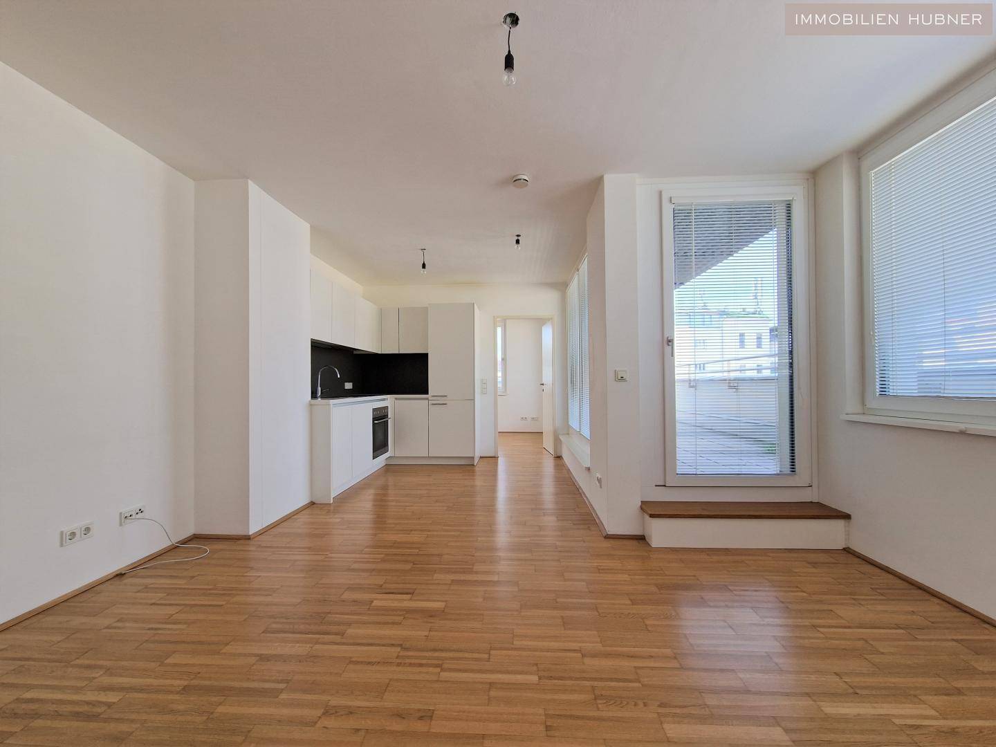 Lichtdurchfluteter Wohnbereich mit integrierter Küchenzeile und Parkettboden, ideal für offenes Wohnen.