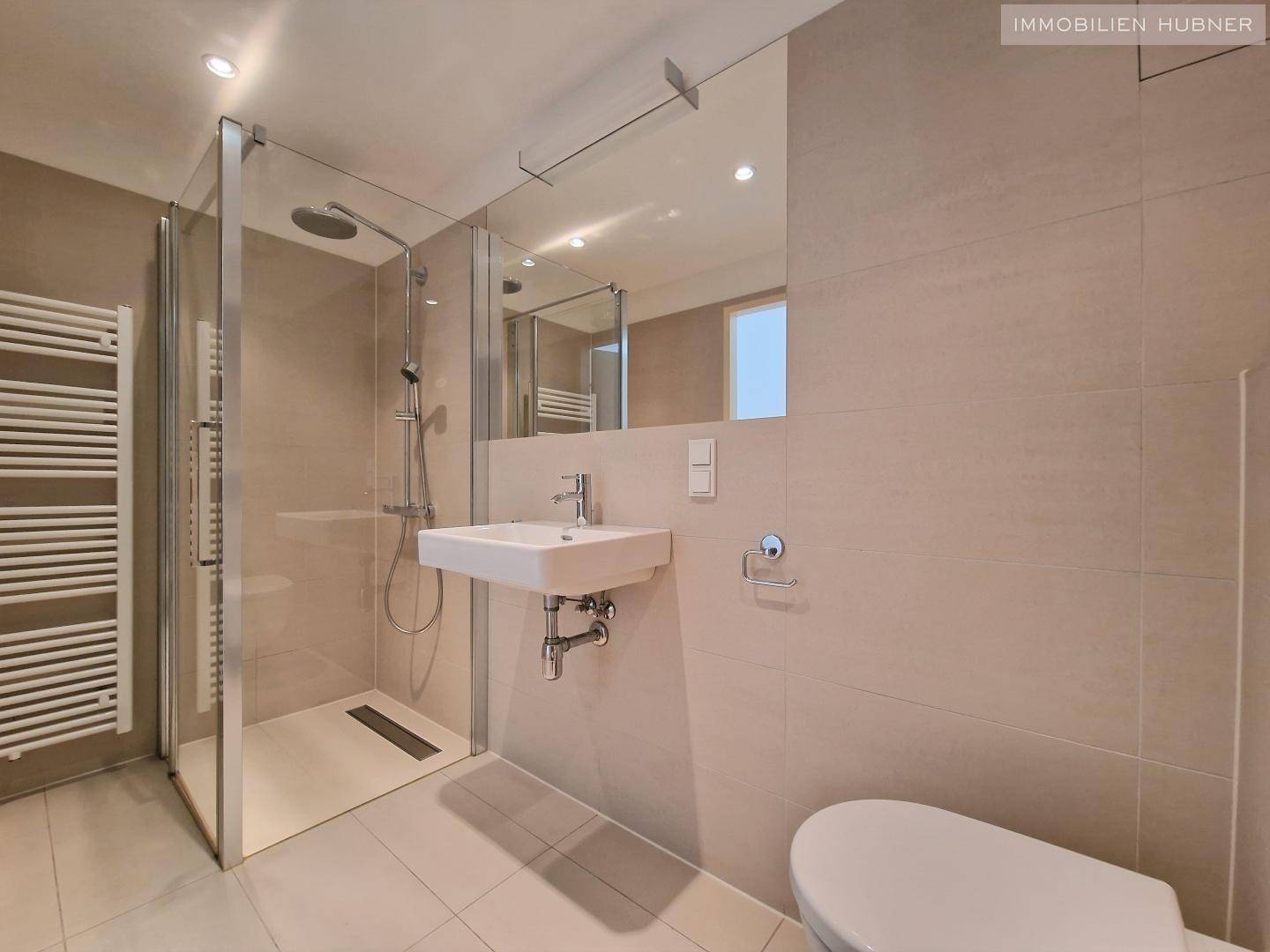 Modernes Badezimmer mit ebenerdiger Dusche, Wand-WC und beheiztem Handtuchhalter in Beige.