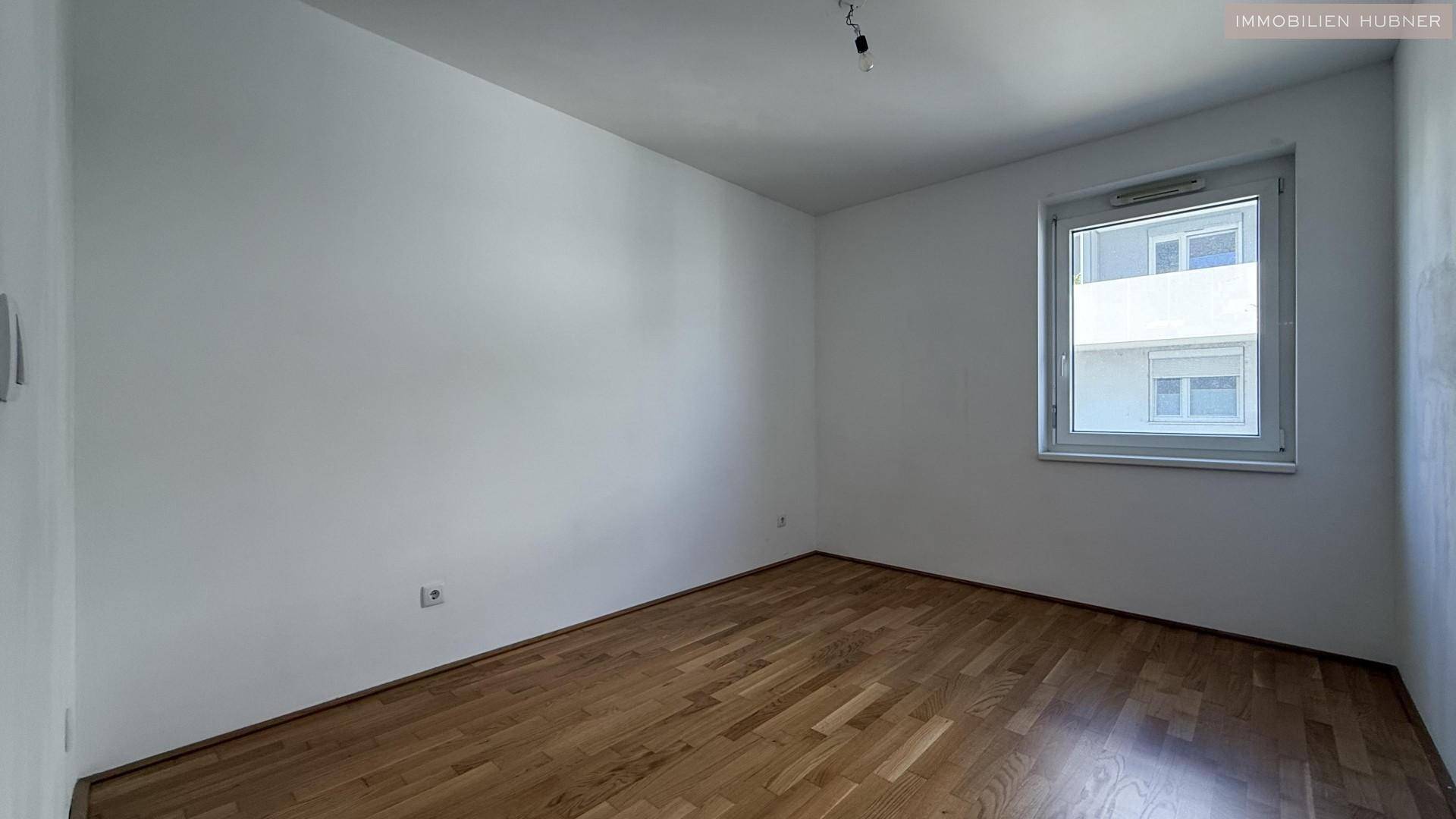 Helles Schlafzimmer mit Parkettboden und einem Fenster mit Blick nach draußen.