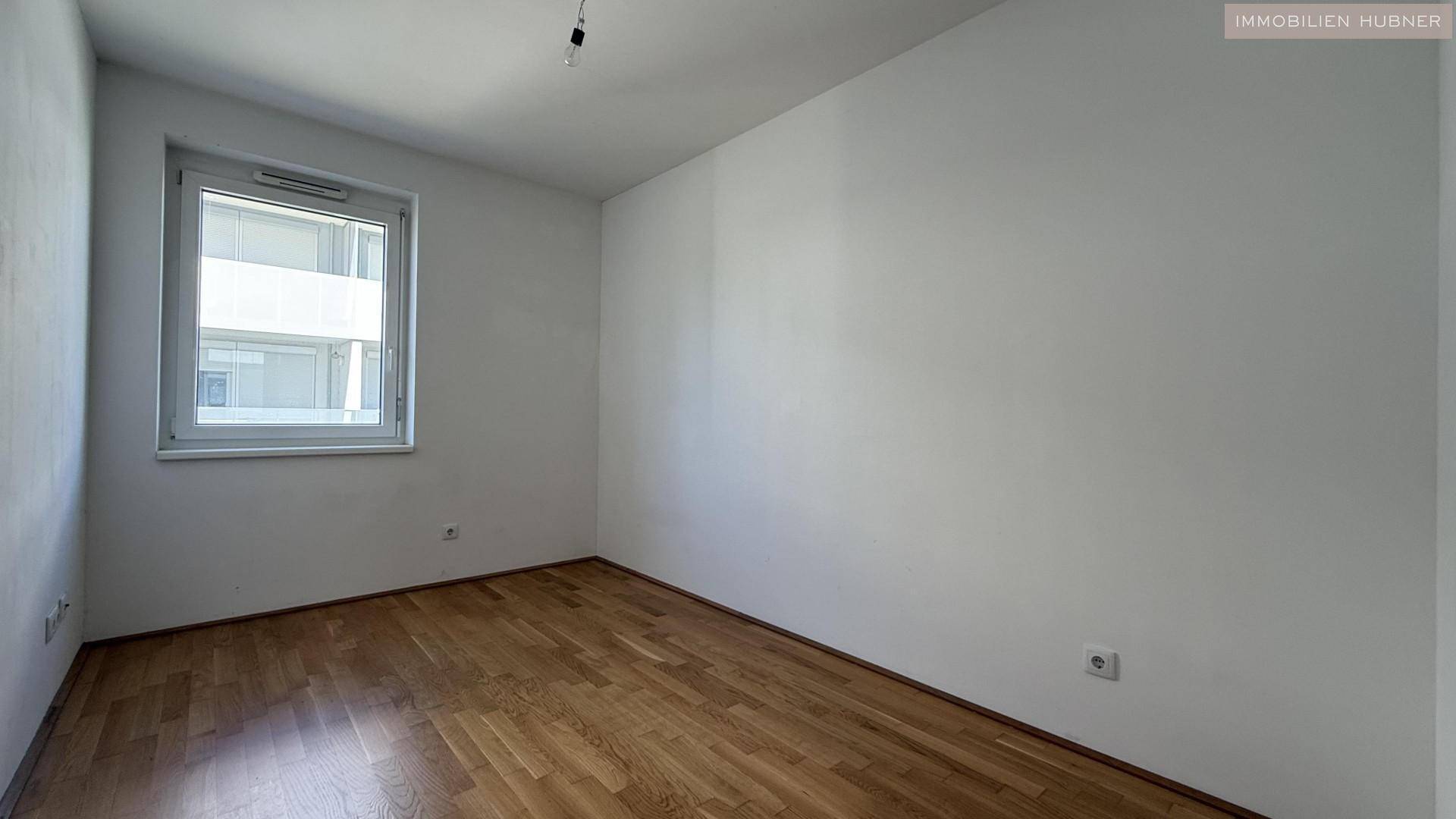 Geräumiges Schlafzimmer mit Parkettboden und einem großen Fenster.