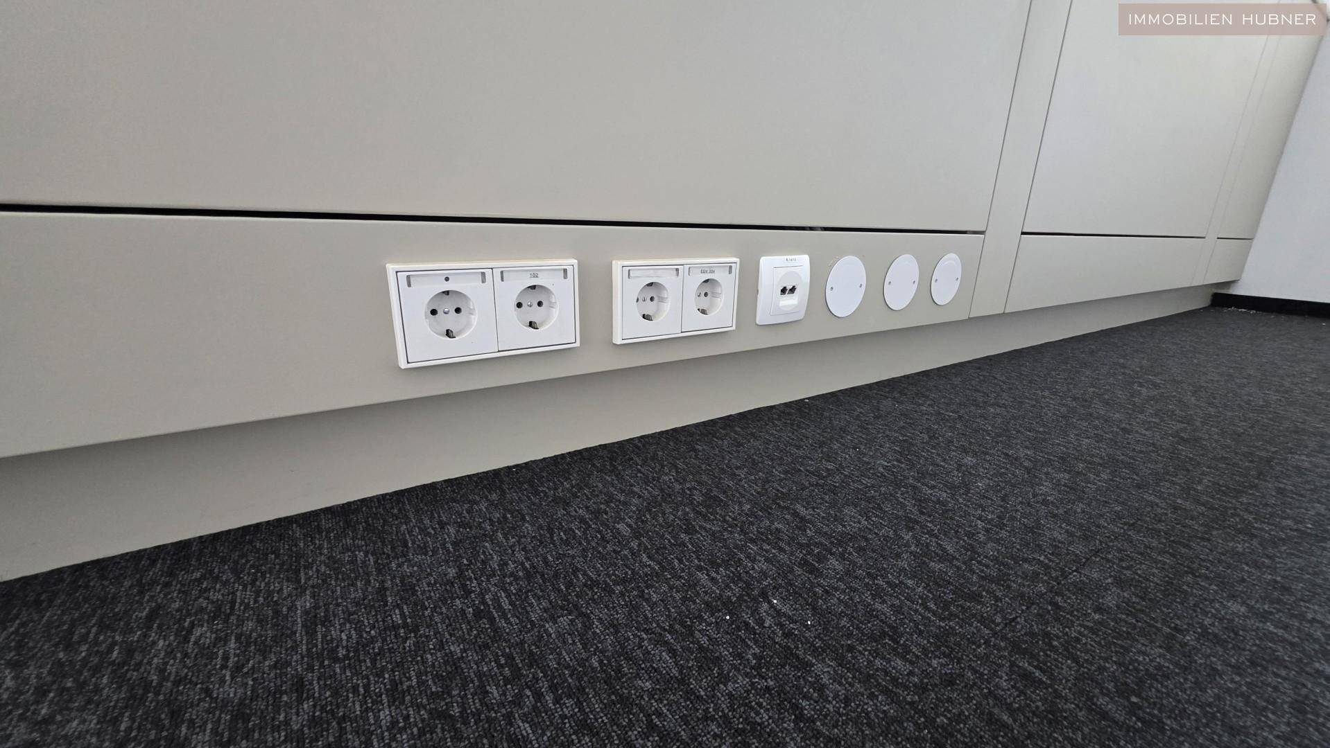 Detailaufnahme von Steckdosen und Anschlüssen entlang der Wand in einem modernen Büroraum.