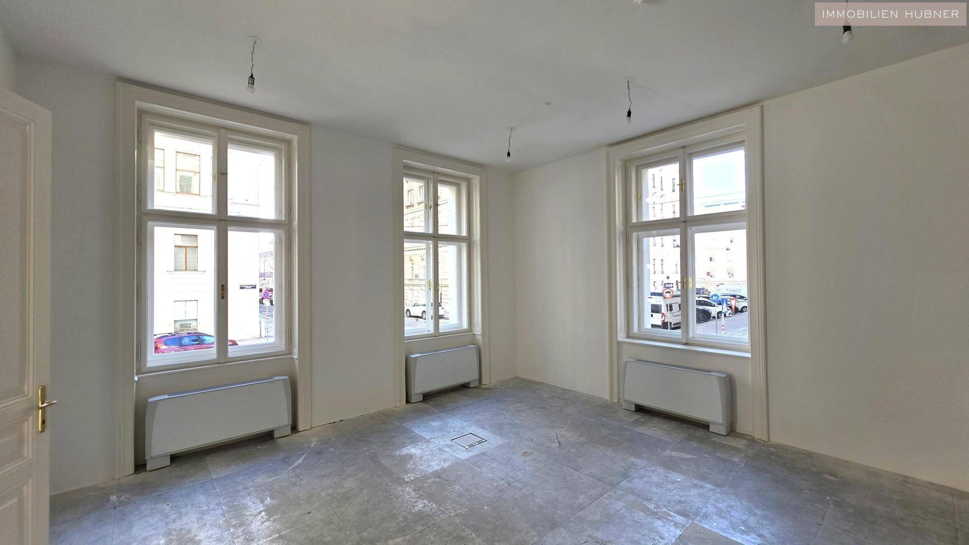 Geräumiger, heller Raum mit drei großen Fenstern und Blick auf die Straße.