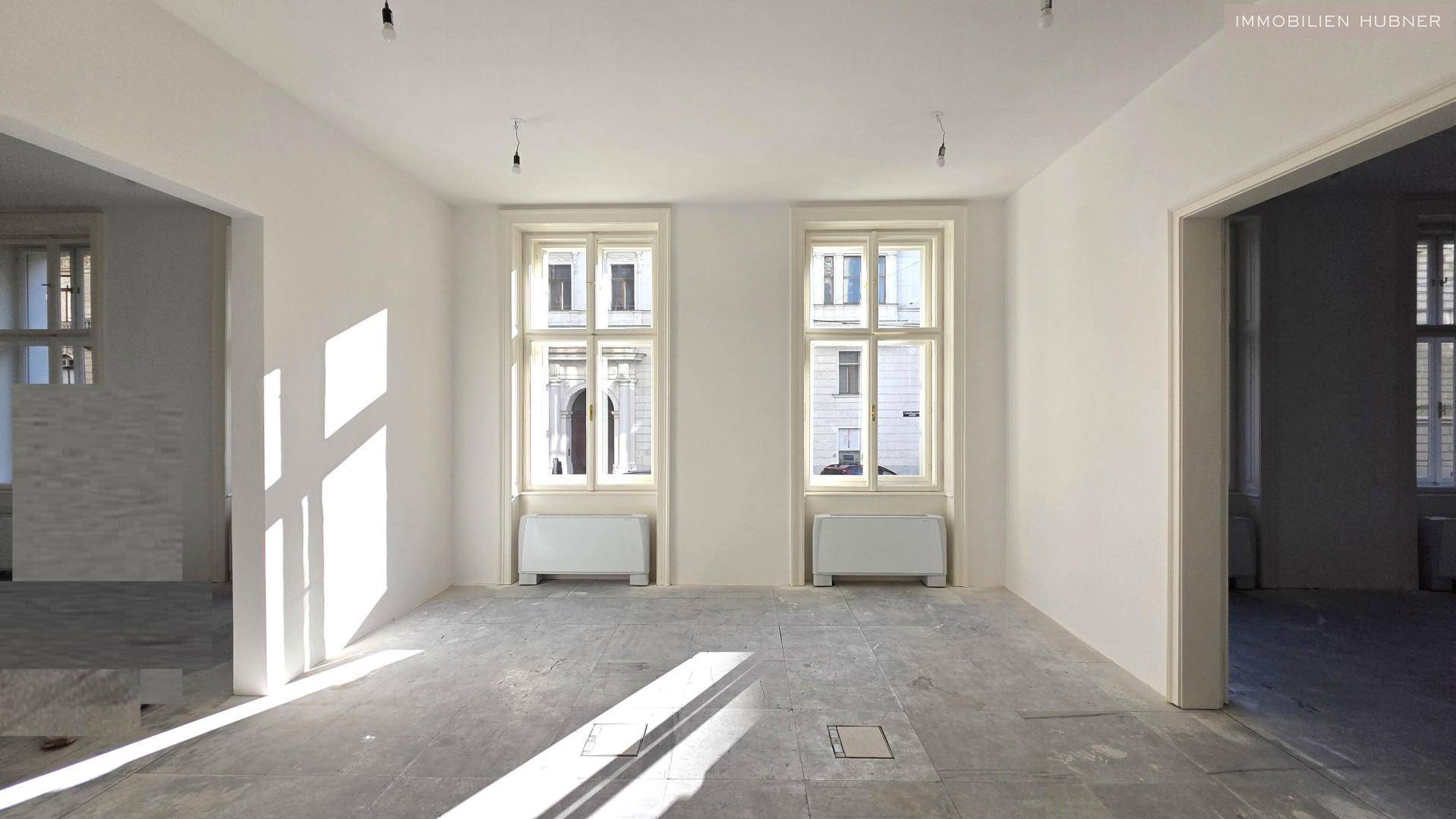 Heller, leerer Raum mit zwei großen Fenstern und Betonboden, ideal für Büronutzung.