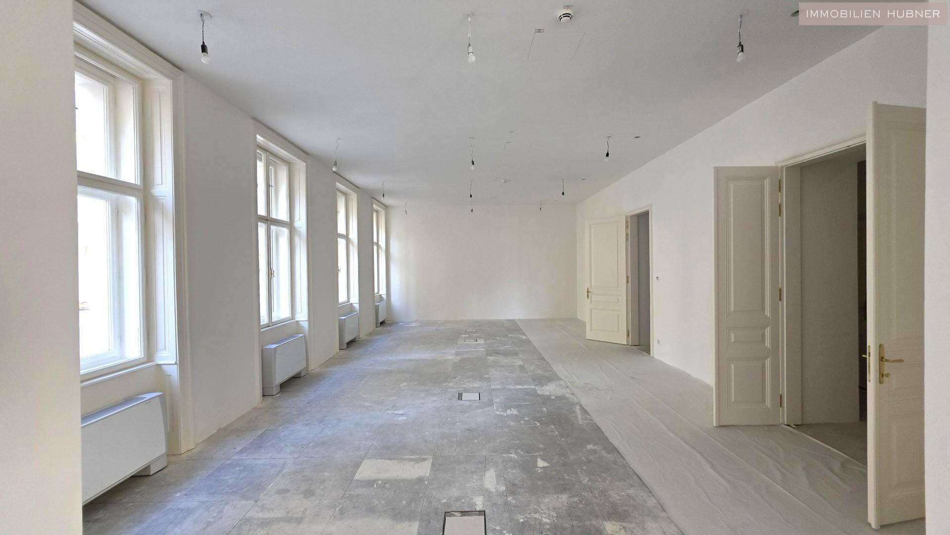Langer, heller Raum mit vielen Fenstern und Betonboden, bereit für den Ausbau.