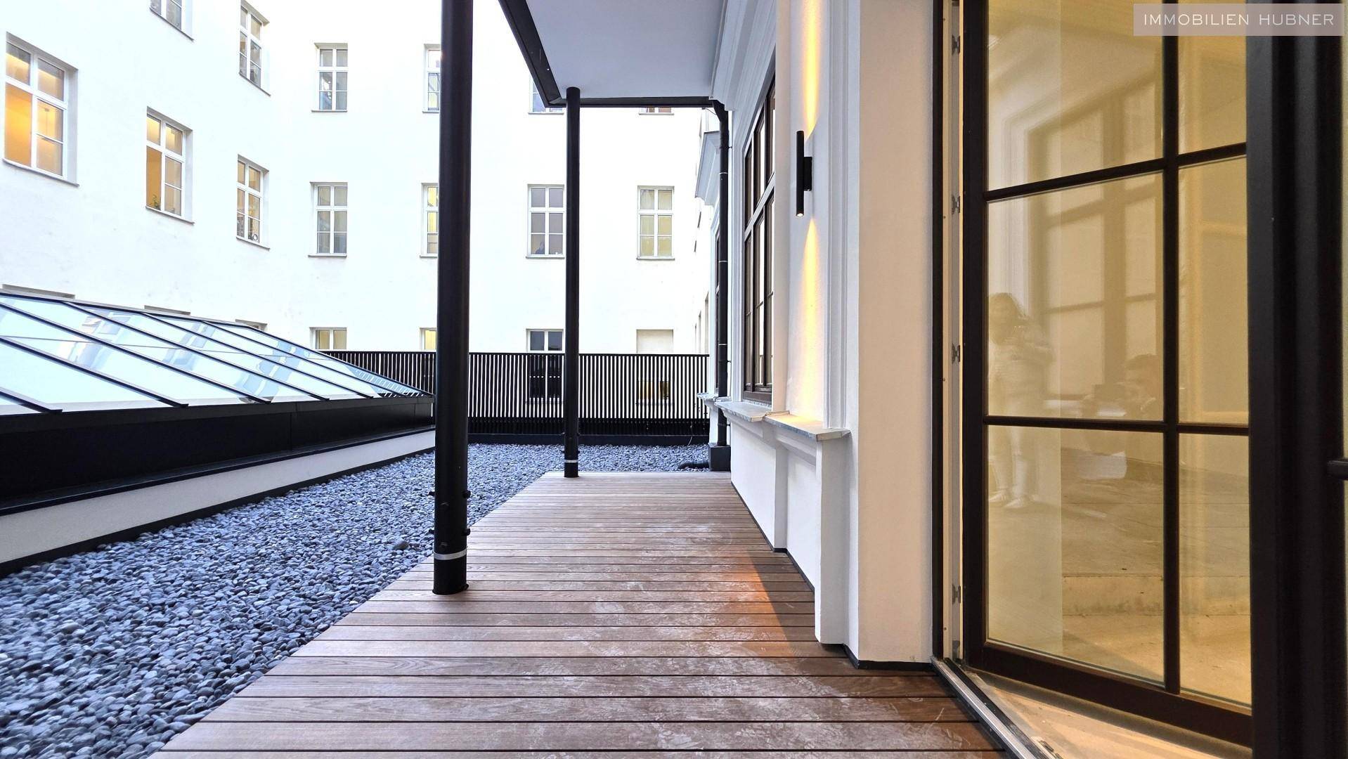 Moderne Terrasse mit Holzdeck und Kiesfläche, umgeben von Gebäuden, bietet einen ruhigen Außenbereich zum Entspannen.