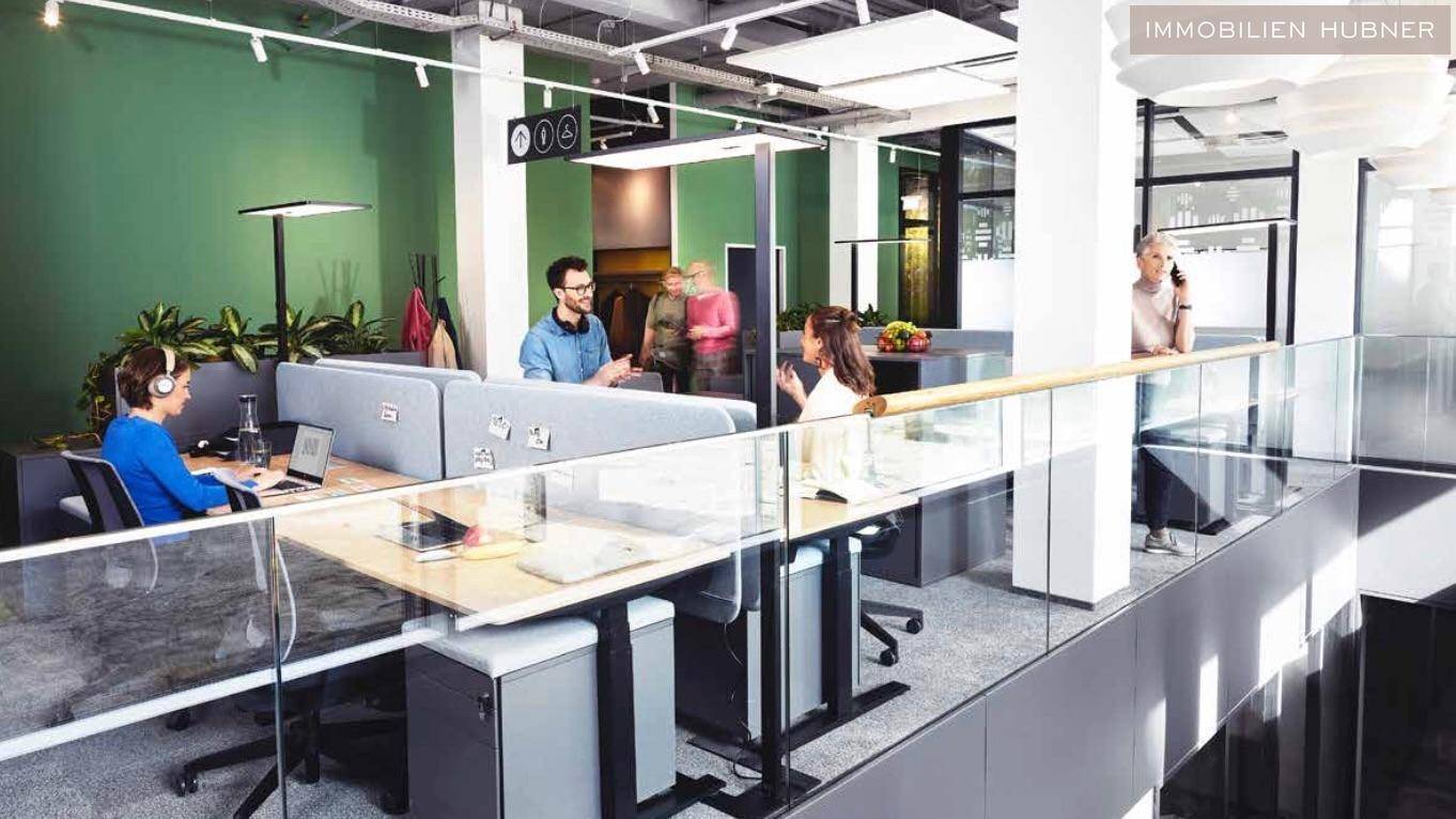 Offener Bürobereich mit modernen Arbeitsplätzen, grünen Wänden und Glasgeländer.