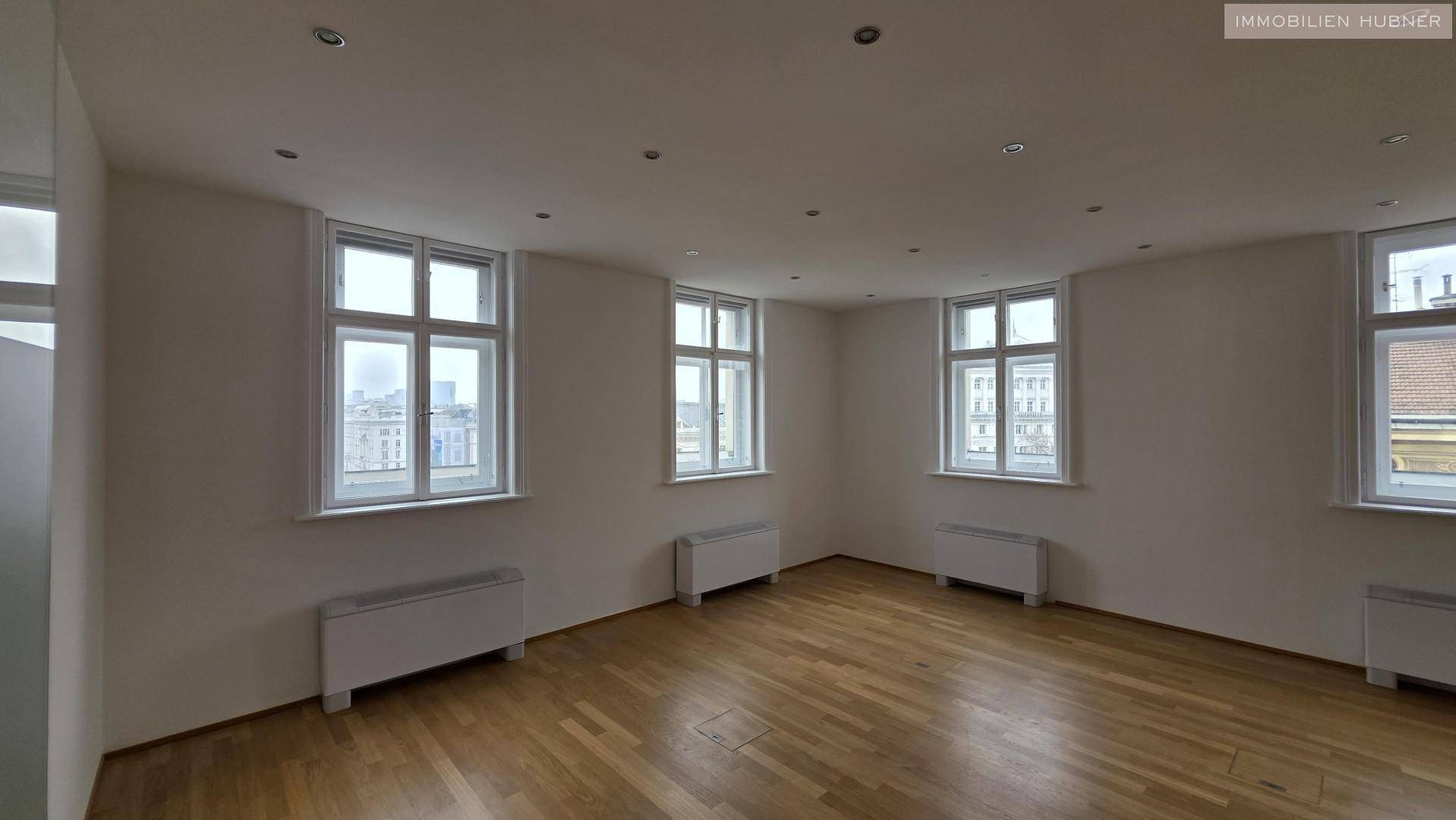 Geräumiges Büro mit mehreren Fenstern, die viel Tageslicht hereinlassen, und einem Holzparkettboden.