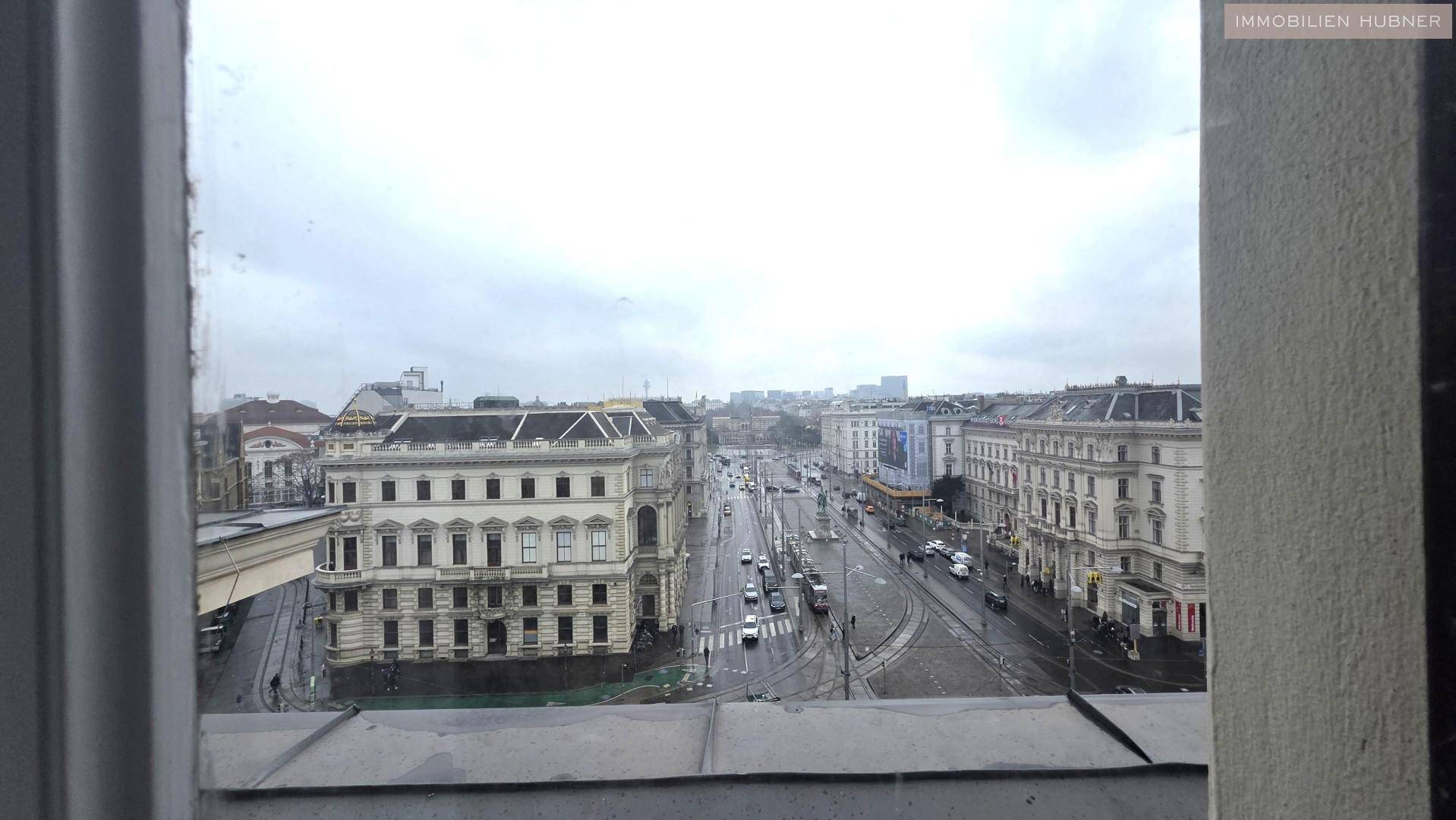 Panoramablick aus dem Fenster auf eine belebte Stadtlandschaft mit Gebäuden und Straßenverkehr.